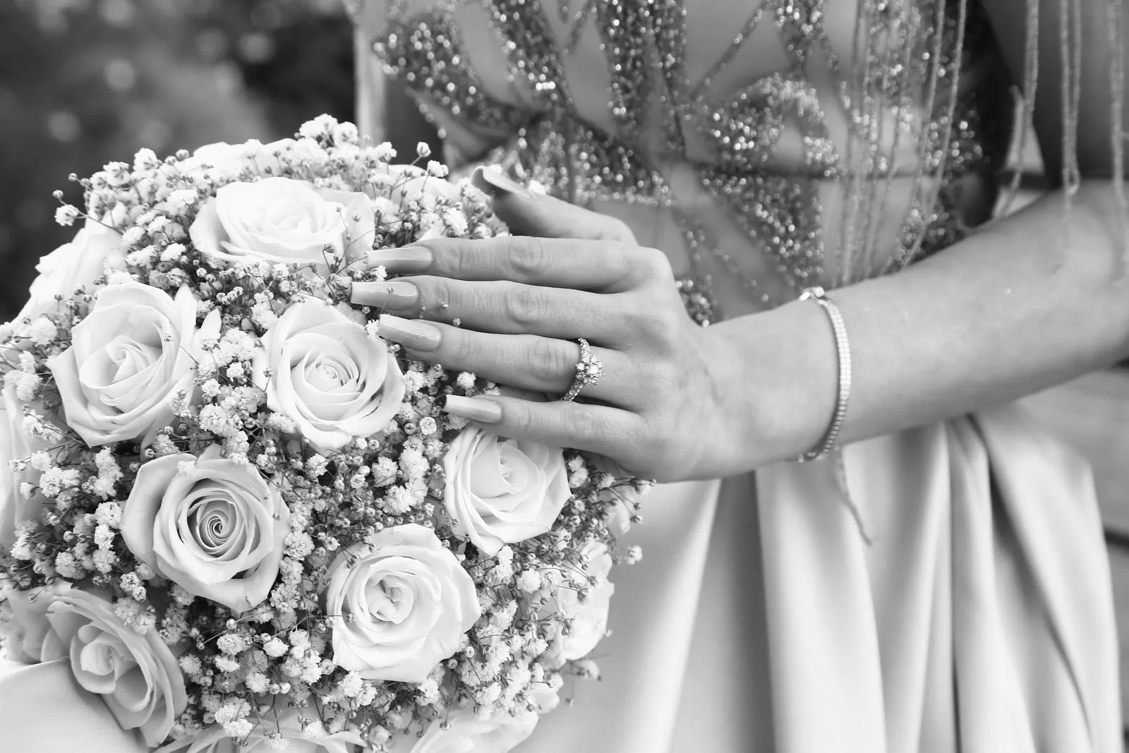 Black and white capture of a bride's hands with a rose bouquet, highlighting the wedding ring.